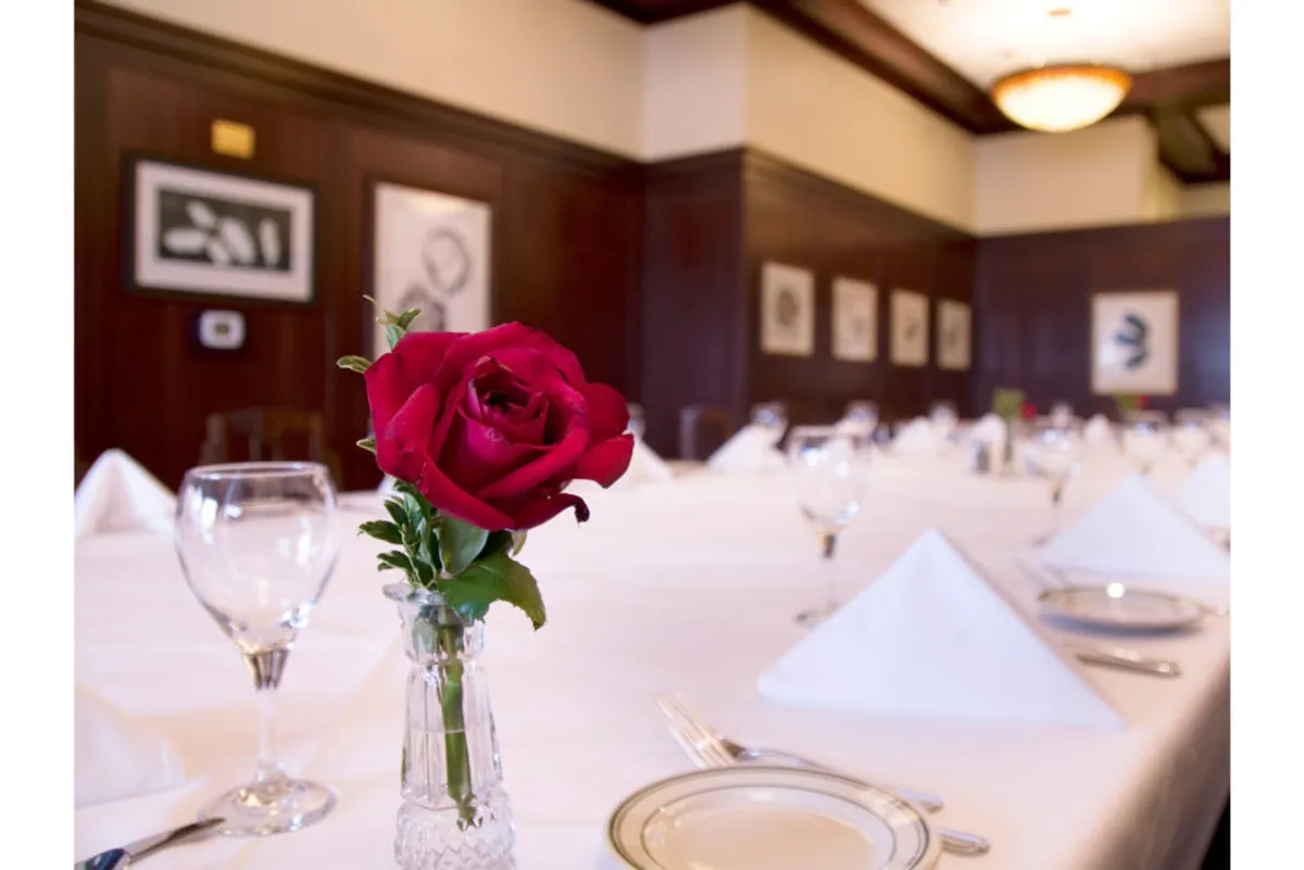 A refined dining table set with a red rose and elegant dinnerware, complemented by framed contemporary artwork in the background. The intimate lighting and sophisticated setting set the stage for a memorable dining experience, whether for an intimate dinner or a special celebration.