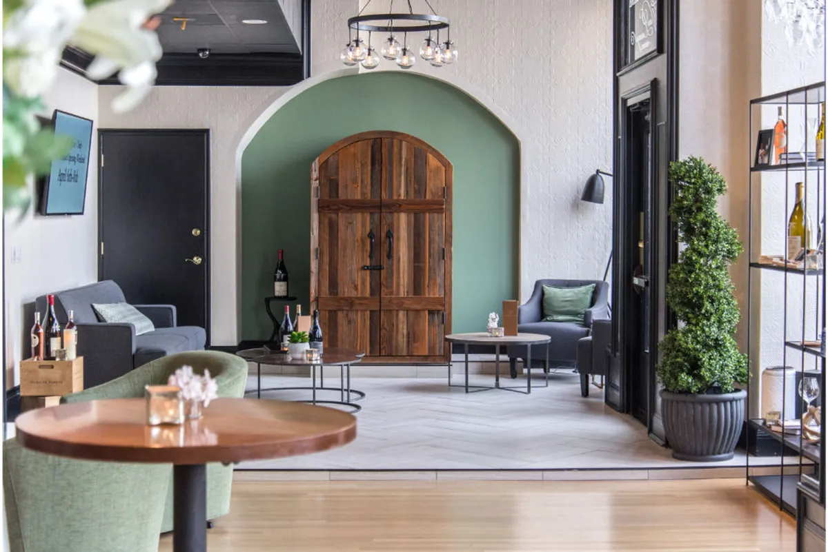 A sophisticated interior featuring a wooden door, green accent wall, neatly arranged furniture, and a shelf stocked with glassware. The space is set up for casual gatherings, wine tastings, and networking, exuding a welcoming yet upscale ambiance.