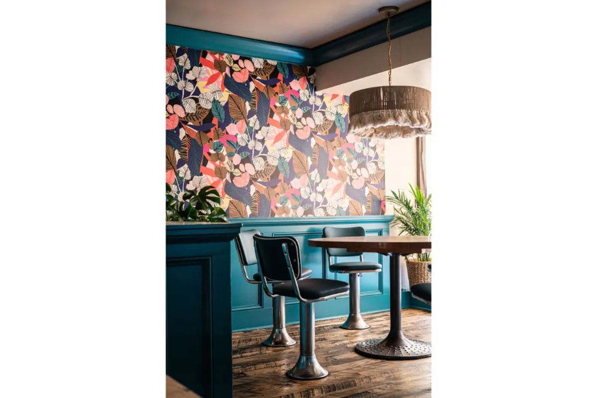 A vibrant dining nook with bold floral wallpaper, a contemporary pendant lamp, a modern dining table, and sleek chairs. The scene is energetic and cheerful, evoking a sense of inspiration and stylish leisure.