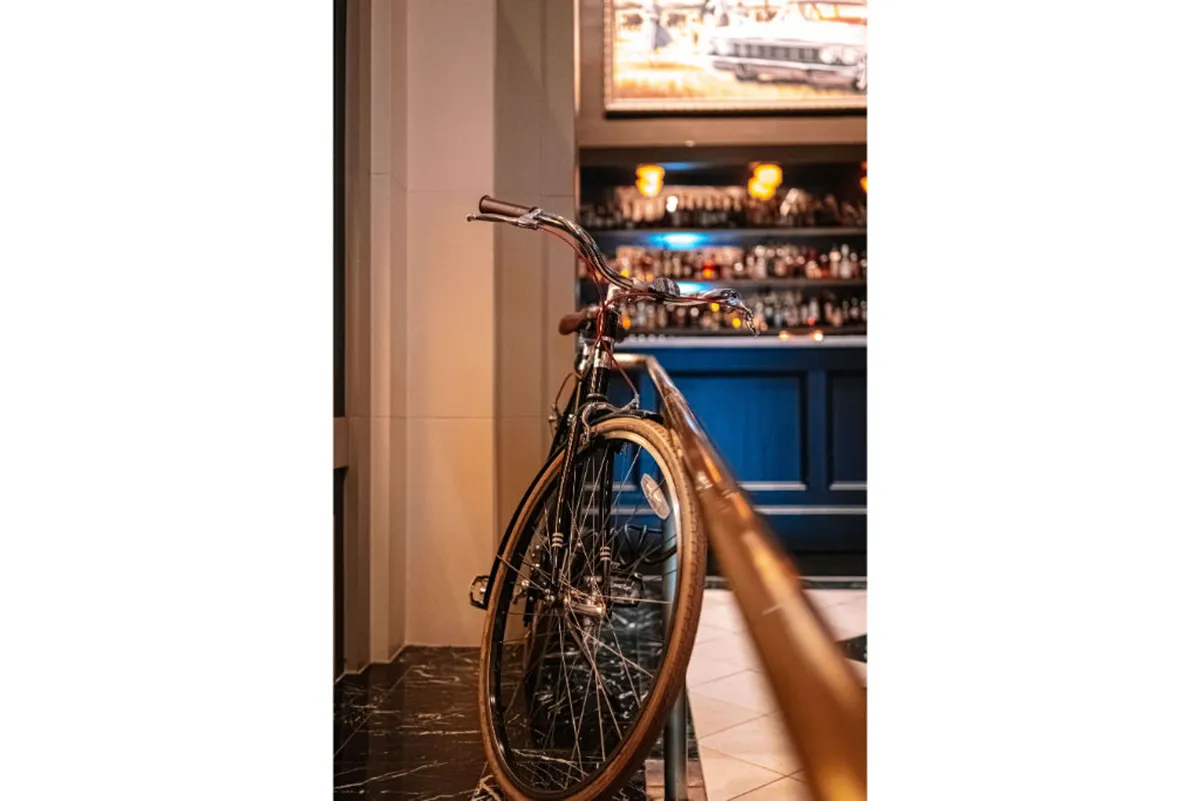 A casually sophisticated bar area includes a bicycle as playful decor, background artwork, and a welcoming bar counter. Lively greenery and eclectic art set the tone for creative socializing, ideal for connecting with other guests over coffee or drinks.