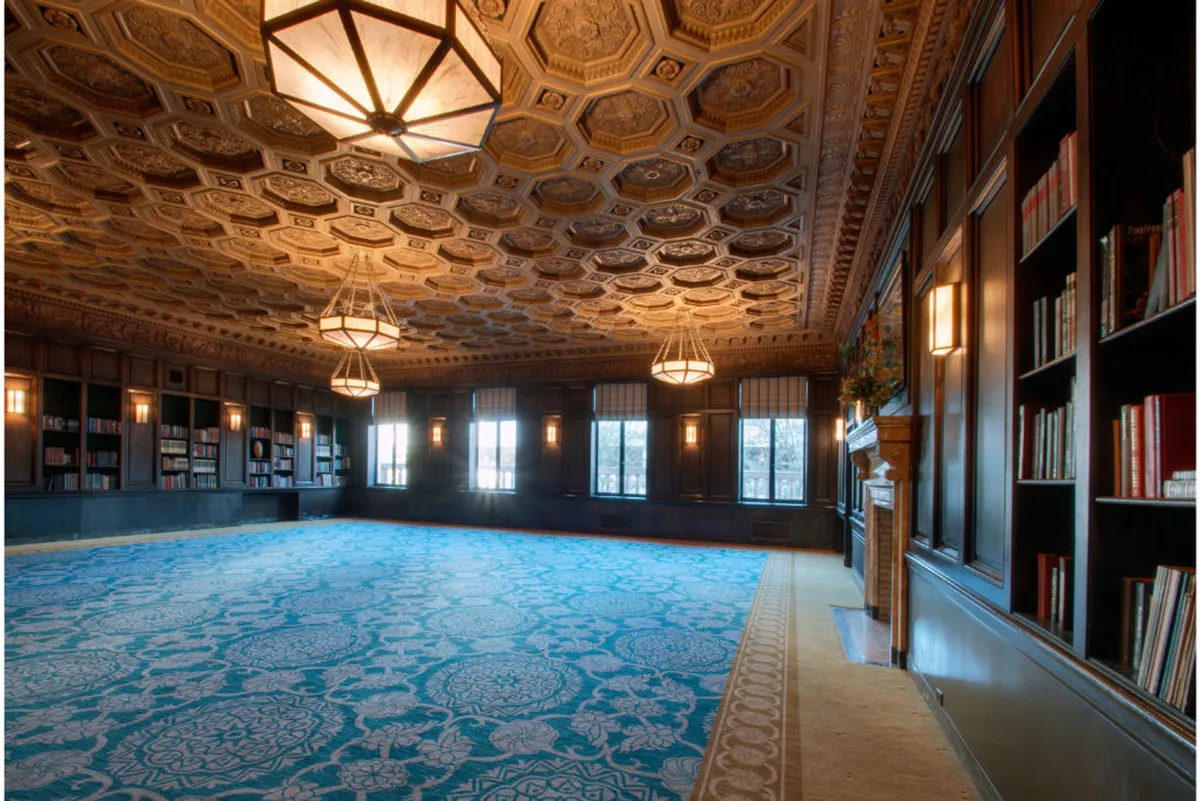 A sophisticated reading lounge bathed in natural light, featuring a grand ornate ceiling, extensive bookshelves, and plush seating. The room’s design encourages both relaxation and contemplation, filled with artistic touches and comfortable arrangements for small group conversations or solitary creative work.