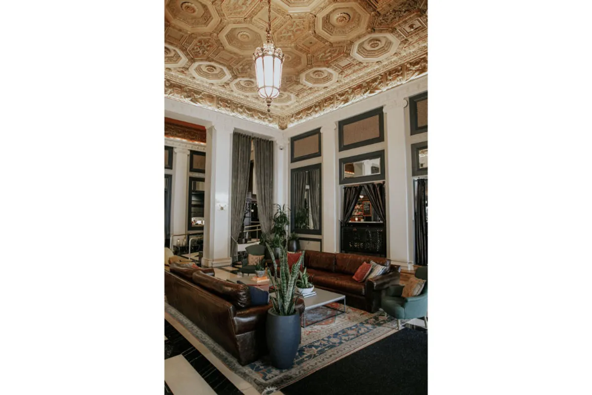 This inviting lounge area features luxurious sofas, chic decor accents, potted plants, and an ornate ceiling. The space is flooded with natural light, creating a warm and comfortable atmosphere ideal for relaxing after exploring the city with a pet.