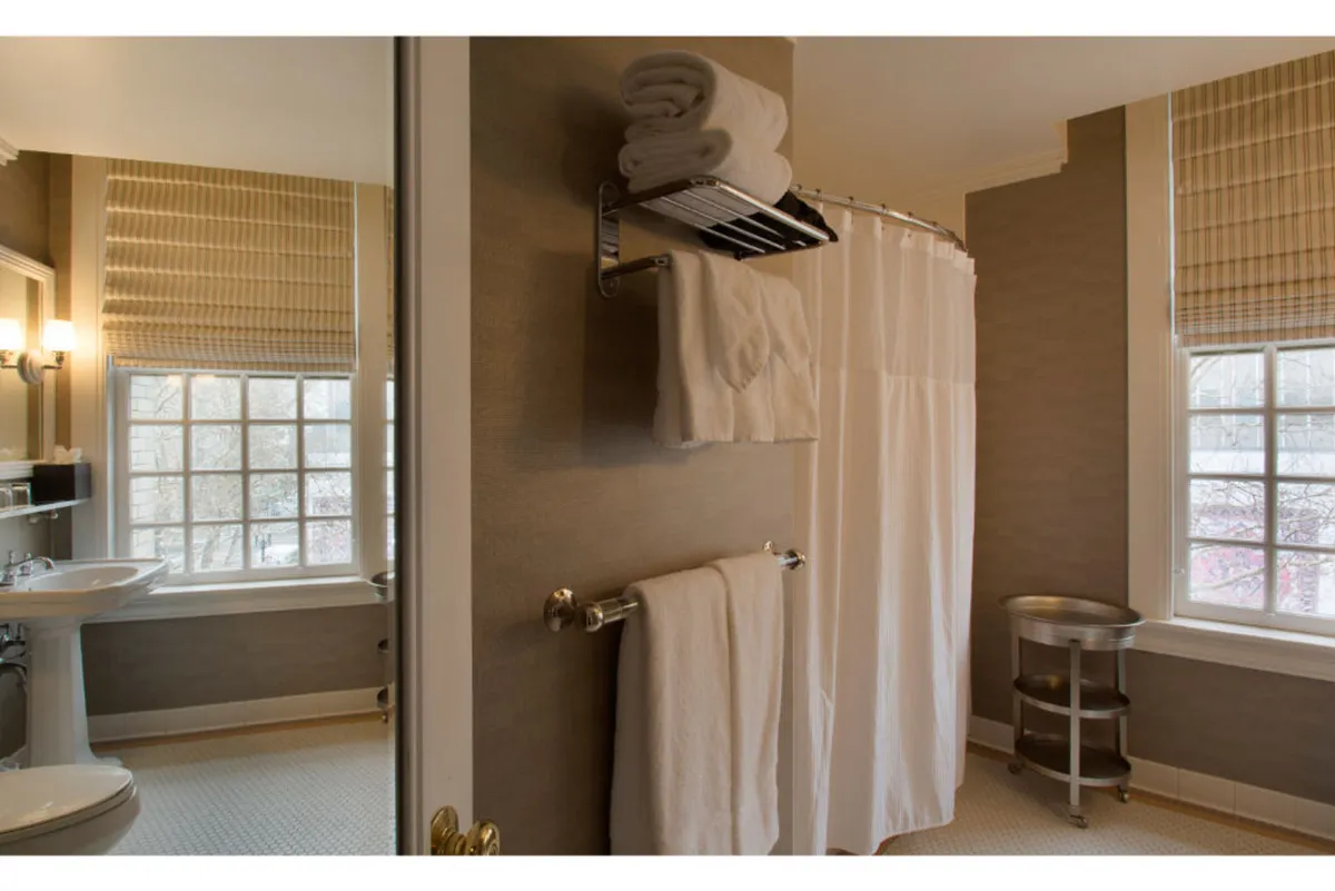 A serene bathroom filled with natural light features a window, a shower curtain, and a towel rack with neatly stacked white towels. The space exudes tranquility and is designed for self-care and rejuvenation.