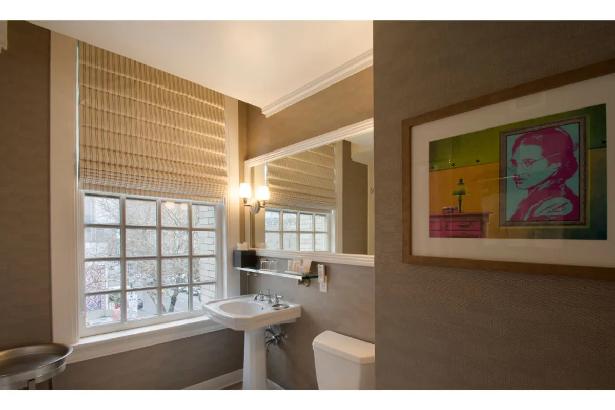 A serene bathroom scene highlighted by a stylish sink, a well-lit mirror, curated artwork, and a window that fills the space with natural light. The setting embodies calm and artistic flair, perfect for moments of personal reflection and relaxation.