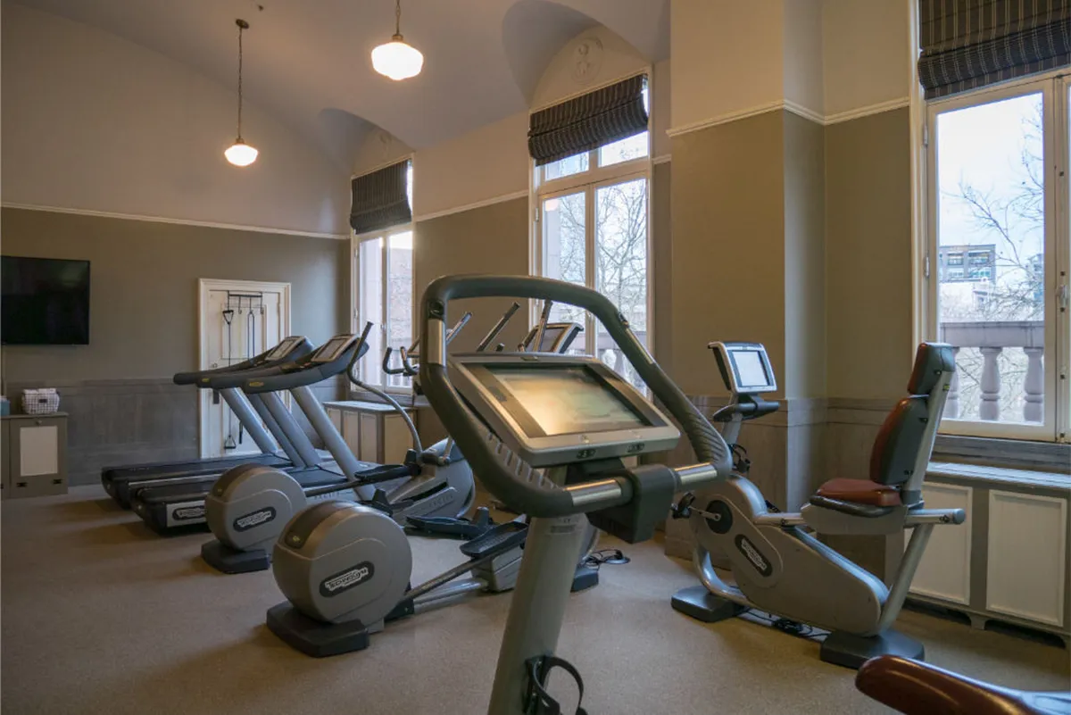 A well-equipped fitness center with multiple treadmills and elliptical machines set before large windows, allowing in vibrant natural light. The atmosphere is energetic and inviting, ideal for maintaining fitness routines.